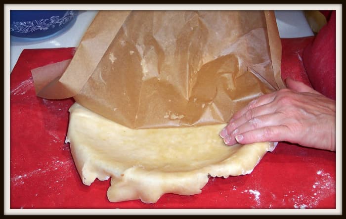 Now carefully peel off the paper. (Here we have parchment.) Bring together any torn edges and seal them. Moistened fingers help. Then, lightly press the dough into the bottom edges of the pie plate.