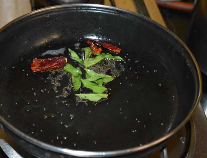 Step two: Heat oil in a deep-bottomed pan. Add mustard seeds. Let them crackle. Throw in broken red chilies and green chilies(optional). Also add curry leaves. Saute for 10 seconds on low heat.