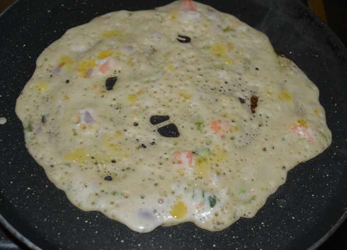 Step five: Heat a pan, preferably a non-stick pan. Grease it with ghee or oil. Pour 1 1/2 ladles of batter in the center. Spread it to make a pancake. Add a few drops of ghee or oil on the top.