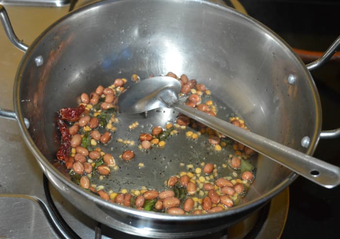 Step three: Heat oil in a deep-bottomed pan. Add mustard seeds. Let them crackle. Throw in Bengal gram dal, urad dal, peanuts, broken dry red chilies, and curry leaves. Saute until peanuts are crispy and lentils turn golden brown.