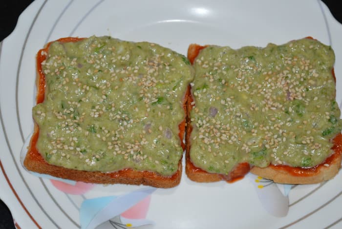 Step four: Generously spread the cheese-moong dal mixture on them. Also, add some white sesame seeds on the top. This will give crunchiness to the toast.