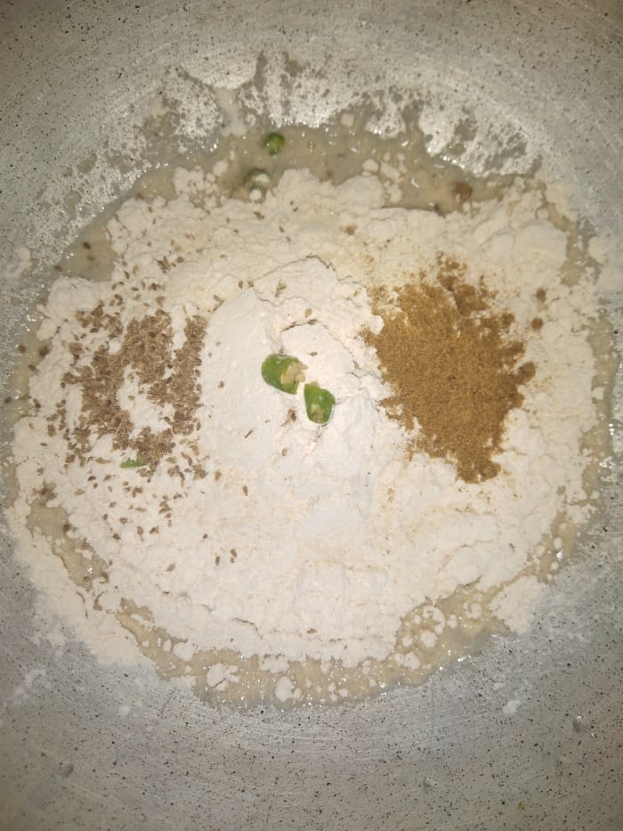 In a bowl, add wheat flour, salt, carom seeds, green chilies (optional), asafoetida (hing) and cumin powder.