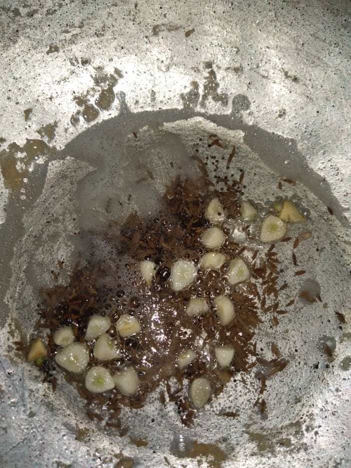 In a pan, heat the oil and add the mustard seeds and cumin seeds. Let them crackle. Add garlic, then fry for a few seconds.