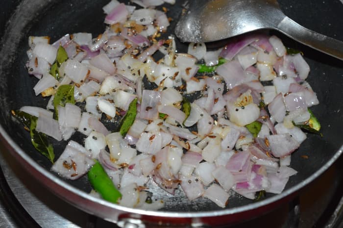 Step three: Add chopped onions, slit green chilies, and some salt. Continue sauteing until onions turn pinkish.