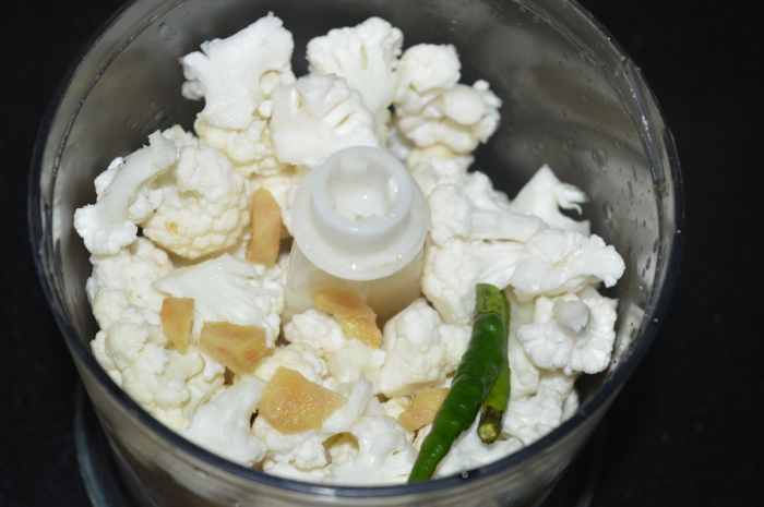 Step two: Wash cauliflower florets. Put them into a food processor along with ginger and green chilies. Finely chop them.