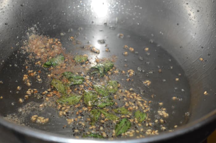 Step six: For making the seasoning, heat the oil in a large pan. Add mustard seeds, sesame seeds, curry leaves, and hing powder. Saute until mustard seeds pop. Turn off heat.
