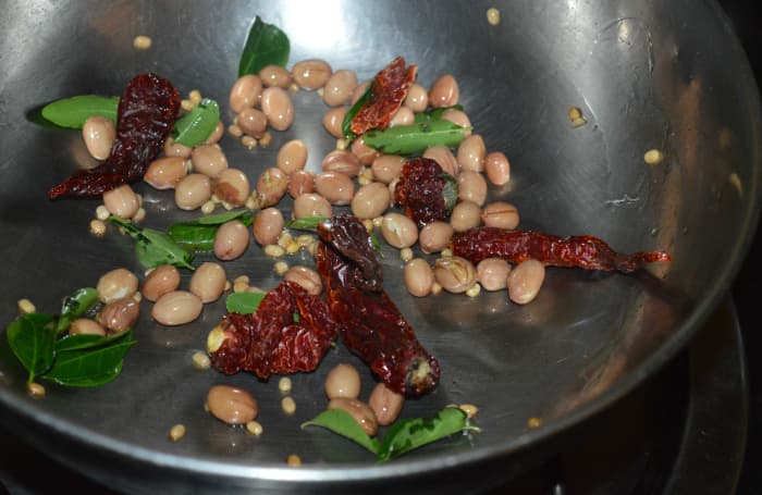Step 2: Heat a teaspoon of oil in a pan. Add peanuts and white lentils. Saute until they become crispy. Throw in curry leaves and broken red chilies. Saute for 20 seconds.