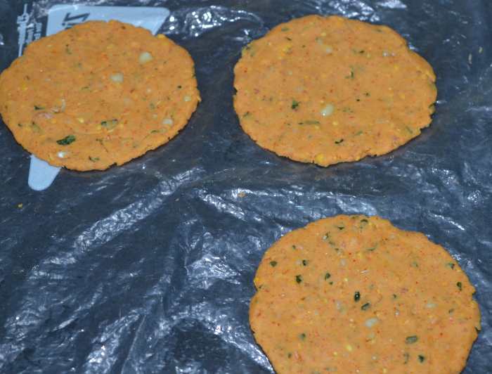 Step 4: Pinch out a lemon-sized portion of dough. Shape it like a patty. Place it on a greased plastic sheet. Pat it with greased fingers to get medium-sized discs; make sure they aren't too thick or too thin. Make 3 such discs.