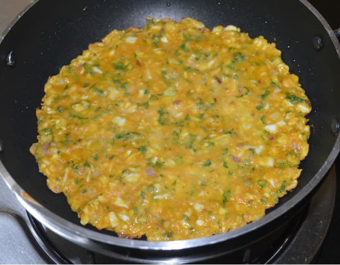Step two: Heat 2 tablespoons of oil in a deep-bottomed nonstick pan. Add the batter in the center. Spread it thickly till the edge. Keep the heat medium-high for a minute. Next, reduce it to medium. Add a few drops of oil on the border.