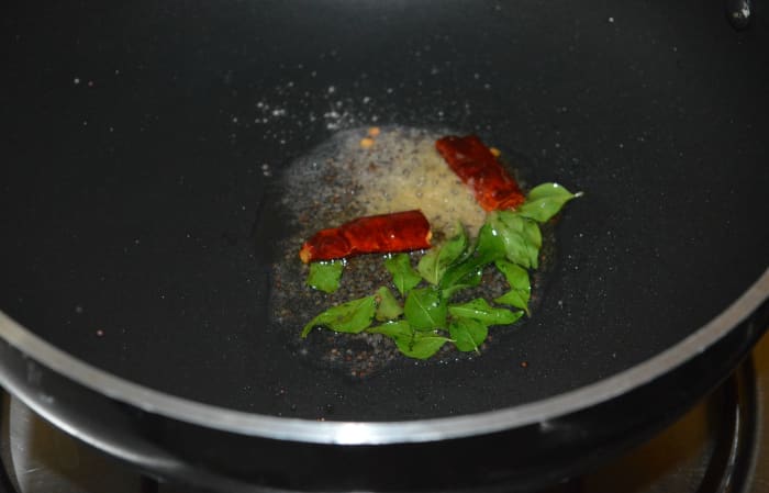 Step two: Add oil in a deep-bottomed pan. Heat it. Add mustard seeds. When the seeds crackle, add broken red chilies, hing powder, and curry leaves. Saute for 10 seconds.