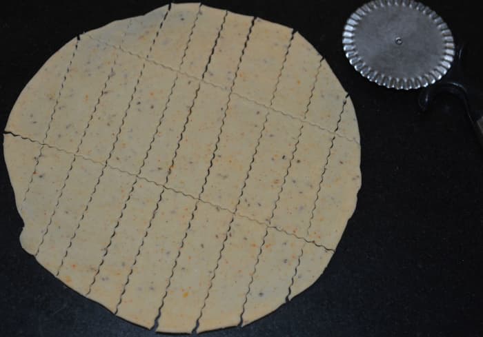 Step two: Take the first dough portion. Make a patty out of it. Roll it out to make a thin disc. With a knife, cut rectangular strips.