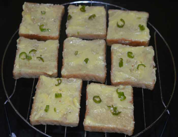 Sprinkle a little bit of salt on all the slices. Add chopped chilies and chopped garlic evenly on the top of all the buttered slices.