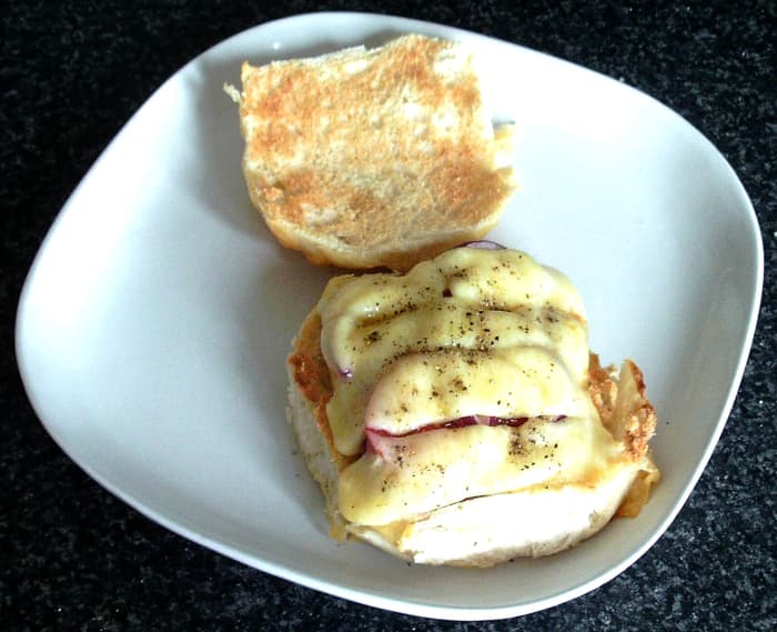Cheese is melted over corned beef, tomato and onion on a cheese crusted bread roll
