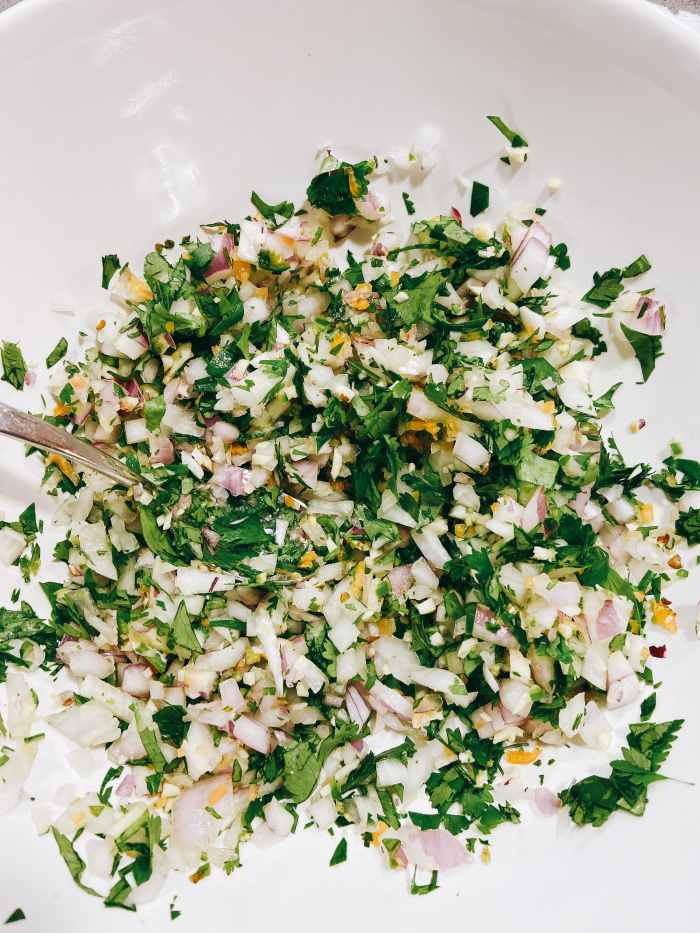 In a large bowl, combine the chopped garlic, onion, cilantro leaves, serrano, and habanero pepper.