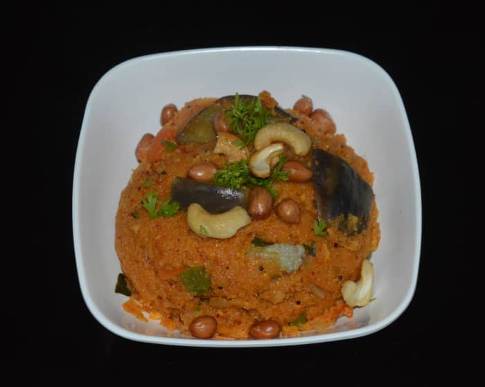 To serve, grease a round bowl. Add the vangibath to the brim. Place a serving plate on it. Invert the bowl and get the round-shaped vangibath on the plate. Garnish it with the roasted cashew nuts, peanuts, and coriander leaves. Enjoy the taste!