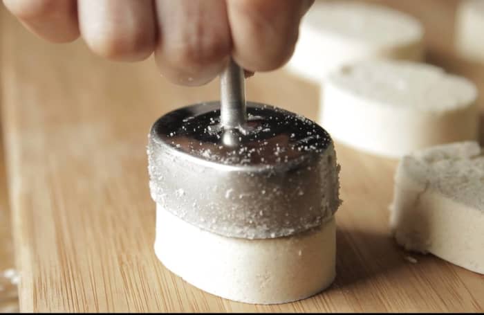 Holding the middle part of the mold with your index and middle fingers and pushing on the plunger with your thumb (like a syringe), push out and release the shaped polvoron mixture onto a baking sheet.