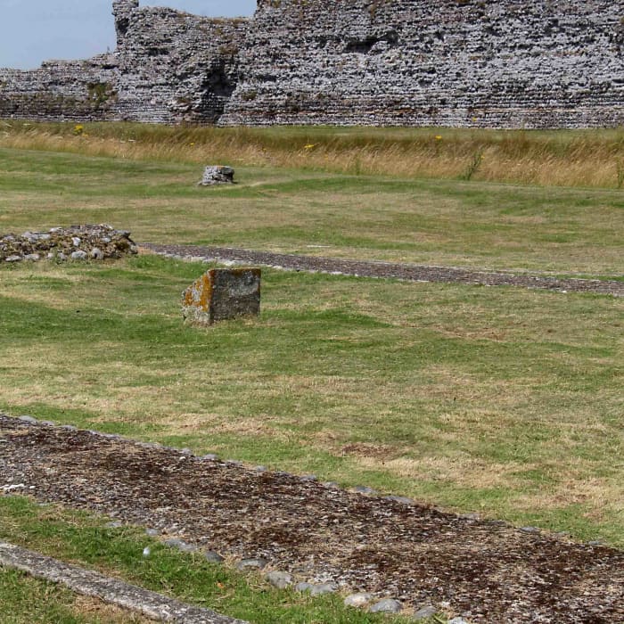 All that remains of the 12th century chapel at Richborough are these foundations and some concrete markers in the foreground. The north wall of the Roman fort stands in the background beyond a trench