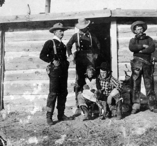 Real cowboys with a girl and a dog in Converse County, Wyoming; costume includes suspenders, bandanas, leather chaps, a pistol, holster, and ammunition belt. They are identified as: "Tom Black" "Chas Mayo" "Tex Biddick" and "Neal Hart."