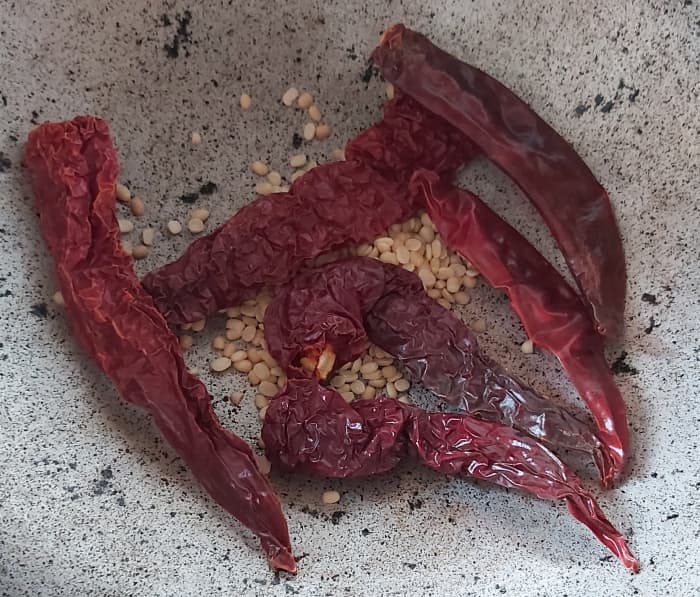 In a frying pan, add 1 teaspoon of urad dal (black split gram), 4–5 Byadagi red chilies, and 1–2 Guntur red chilies (or any red chilies to give color and spiciness). Fry till urad dal turns golden brown and red chilies turn crisp.