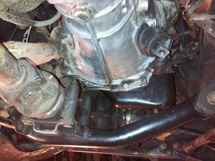 Transmission with hydraulic clutch cylinder installed. The crossmembers are the front differential which tucks up beneath the oil pan. The engine cannot be pulled forward until the differential is lowered or removed. Transmission drain plug visible