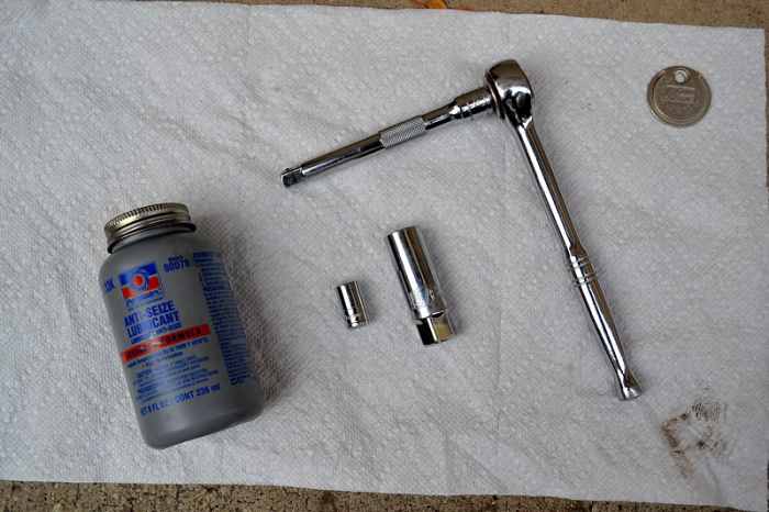 The tools, from left to right: bottle of anti-seize lubricant, a 10mm socket, a 5/8 inch spark plug socket, a 3/8 drive ratchet with a 5 inch extension bar, and a spark plug gap tool coin.