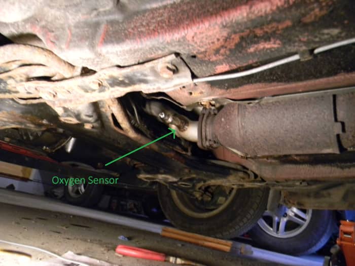 The underside of my Volkswagen Golf mk3 with the pre-cat oxygen sensor being pointed to. I've already cut the wiring off in this picture.