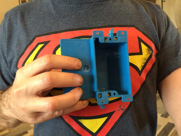 Superman and a Carlon B117RSW Work Outlet Box, one gang, 3.64-inch length by 4.07-inch width by 2-inch depth.