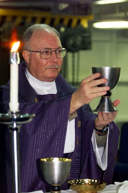 A priest at the altar prepares to serve communion to his congregants who are in need of healing and spiritual guidance.