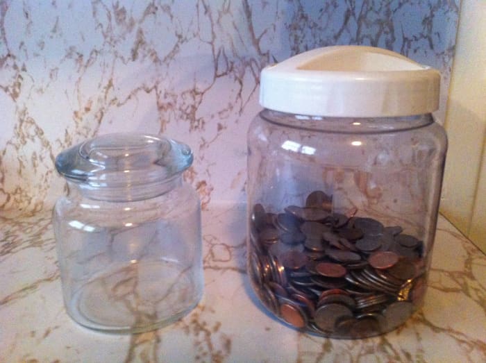 The coins from the jar are moved to the larger container, presenting an opportunity to fill it with more change.