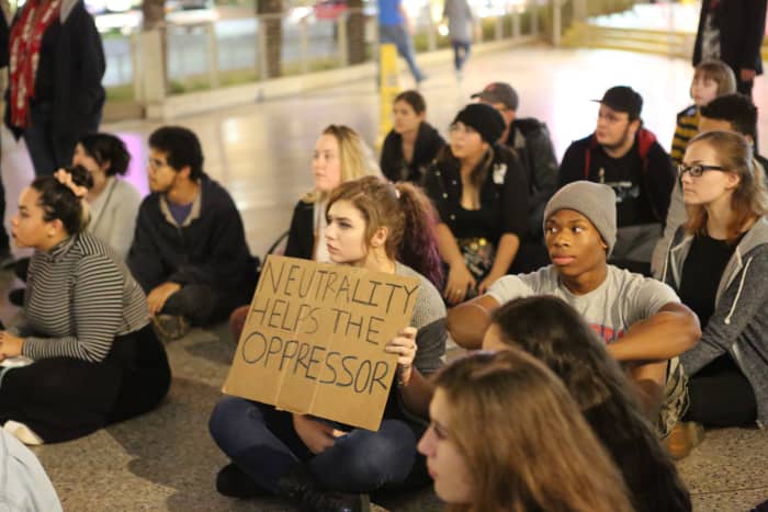 The young woman's sign references a famous quote by humanitarian and political activist Elie Wiesel: "We must take sides. Neutrality helps the oppressor, never the victim. Silence encourages the tormentor, never the tormented."