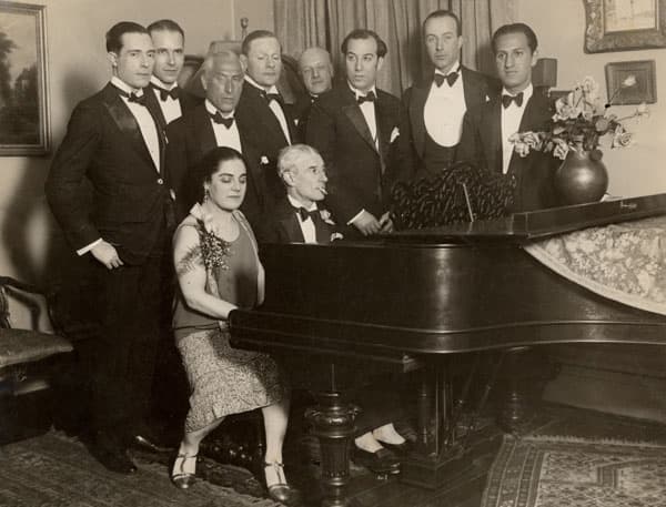 Maurice Ravel 1875-1937. The photo was taken at an evening soiree at the home of Eva Gauthier given in honour of Ravel's birthday in 1928. Ravel is seated at the piano. George Gershwin is one of the guests arranged around it, on the extreme right.