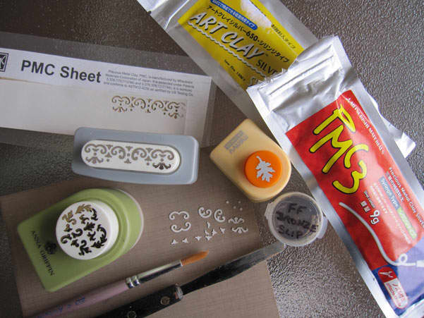 Metal clay syringe, metal clay slip, palette knife, brush and PMC Sheet appliqué cutouts made with paper punches