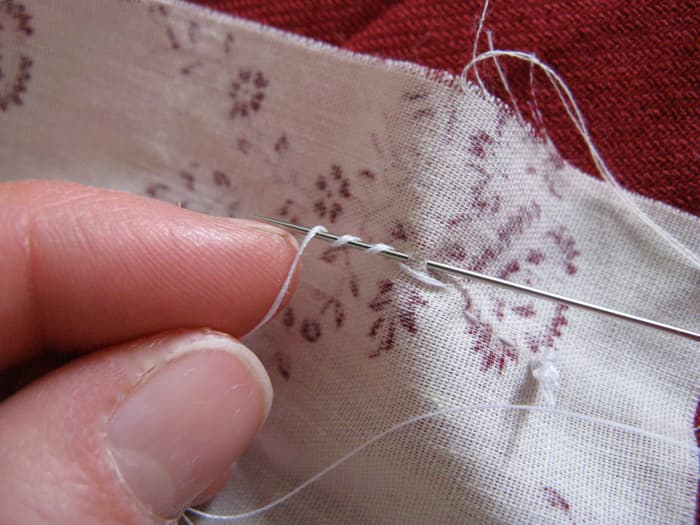 Twist the thread that comes directly out of the cloth (not the end coming out of the eye of the needle) around the sharp end of the needle.