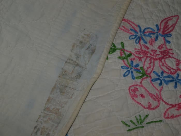Antique quilt with damage from adhesive tape used to hang the quilt. The tape was removed but the glue remained, as well as the tear that occurred when removing the tape.