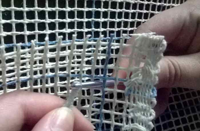 Using a crochet hook or other instrument, pull one of the long strands of yarn from your pom pom through one of the squares in your canvas. Notice how the intersection of the blue lines forms an X shape.