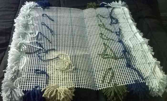 Bottom of yarn pom pom rug in progress. Your rug will look something like this while you're tying the pom poms to it.