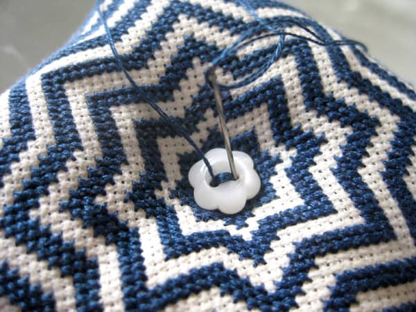 Sewing on one button (the needle passes through to the other side of the biscornu and sews on the second button at the same time).