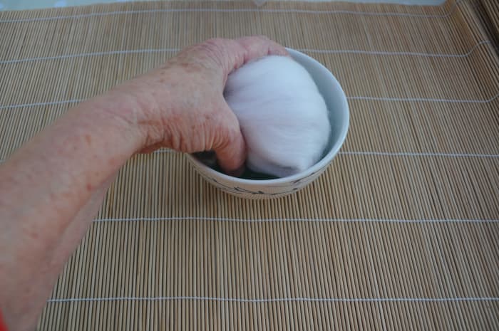 Wet all sides of the wool covered polystyrene ball by dipping each side lightly into the hot soapy water.