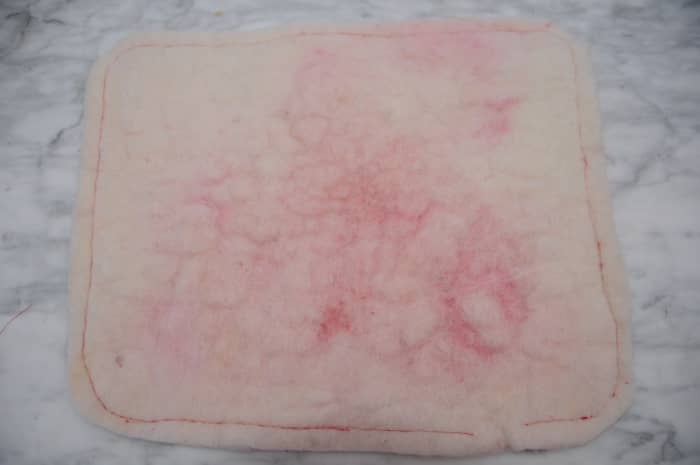 The back of the heart shaped cushion showing how red the white wool looked even after needle felting. The front is now snow white.