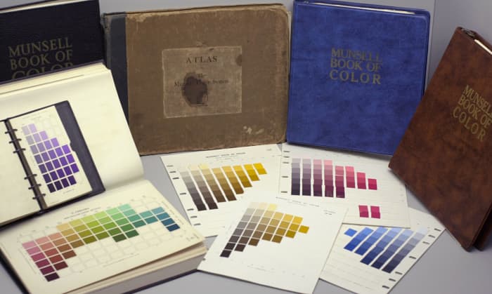 Several editions of the Munsell Book of Color, the color atlas of the Munsell color system sold by the Munsell Color Company, perched behind several of the book’s removable pages of color swatches.