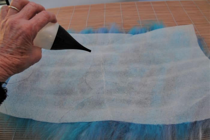 Wetting the surface of the underfloor layment to facilitate easy flattening of the fibers below.