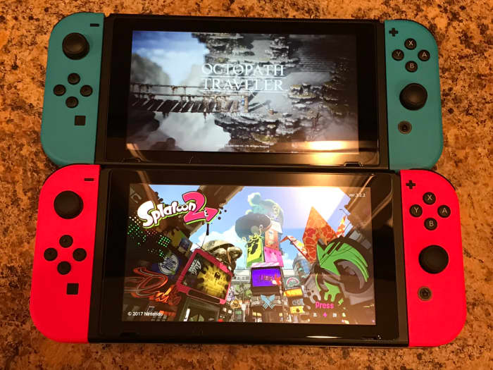 Two Nintendo Switches. The top shows Octopath Traveler and features two neon blue Joy-Cons. The bottom shows "Splatoon 2" and features two neon pink Joy-Cons.
