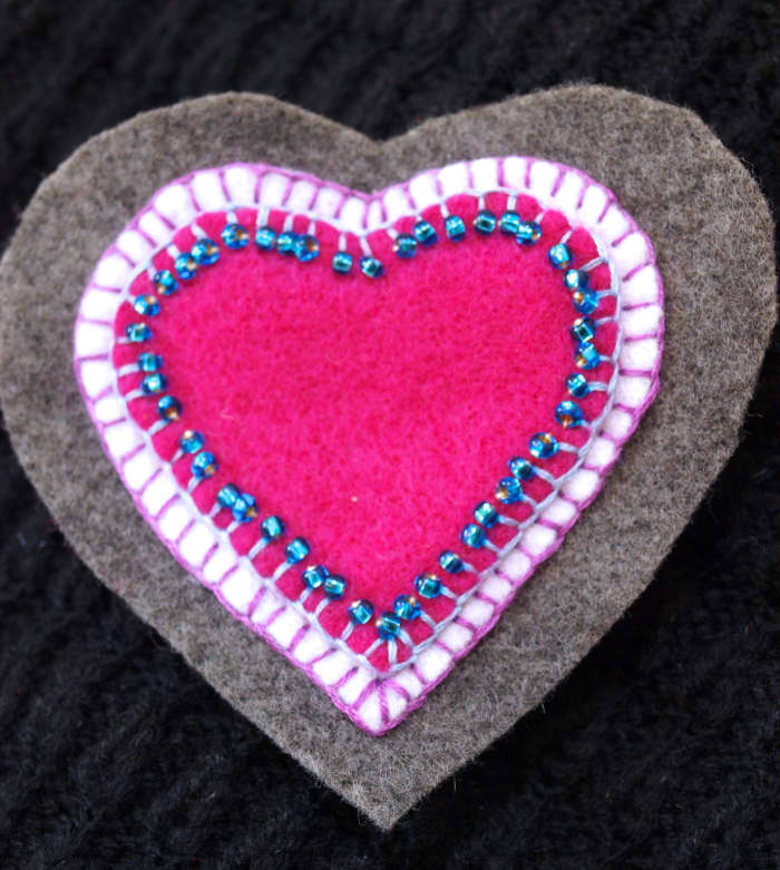 Here's another brooch using the same steps—a heart-shaped felt brooch. I used a blanket stitch for all the layers and added the blue beads after I had stitched the pink heart to the white heart.