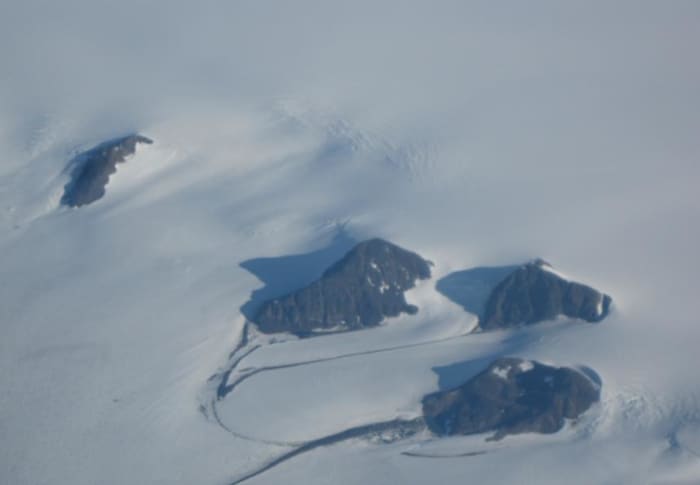 Aerial photo of Mountain Peaks protruding above the Greenland ice cap.
