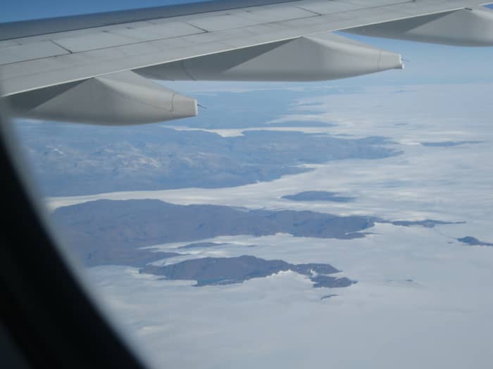 Mountains and lakes in southern Greenland beneath the wing of a jet liner.