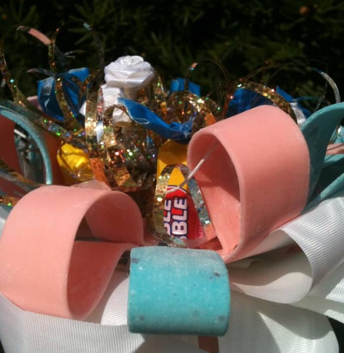 A close-up, inside view of the candy corsage showing the tape and tube forms of bubble gum, tiny white silk flowers, satin ribbon, and a recycled metallic "fountain" bow.