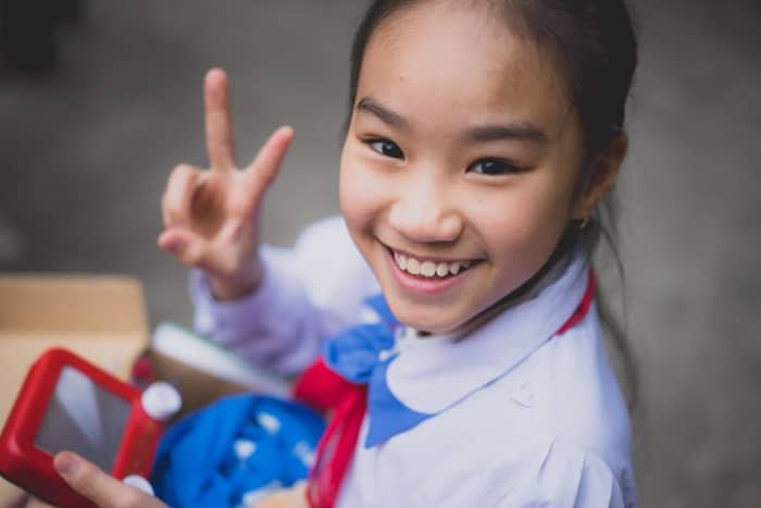 A girl holds up a peace sign while playing with the Etch-a-Sketch from her shoebox.