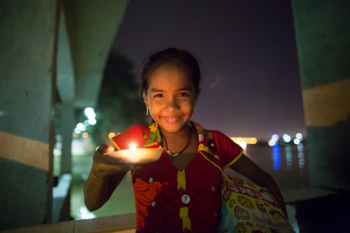 A girl lights the way with a candle while carrying her shoebox home in a village where electricity is scarce and unreliable.