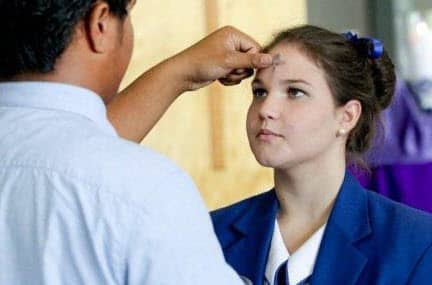 A member of the clergy applying ash in the form of a cross to a woman's forehead.