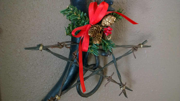 This ornament was made from barbed wire cut into strips and held together with florist wire. A bow and a bit of garland add festive color and charm. Hang on a wall or lower branches of the tree.